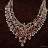 Long necklace with pave CZ scrollwork, pear-shaped red stones and pearl drops on dark brown fabric