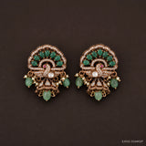 Pair of victorian buttalu earrings with peacock motif, green stone clusters and pearl drops, on dark brown background