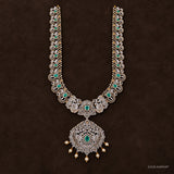 Green stone long necklace with peacock motifs and pearl drop pendant on dark brown background