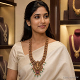 Woman in cream saree wearing a long gold-toned Kundan Nakshi necklace with goddess pendant and green bead drops