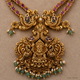 Close-up of the pendant showing a carved deity figure, peacock motifs and pearl-green bead drops