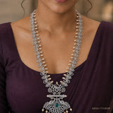 Close-up of the neckline showing the long necklace's floral links and pendant with green stone