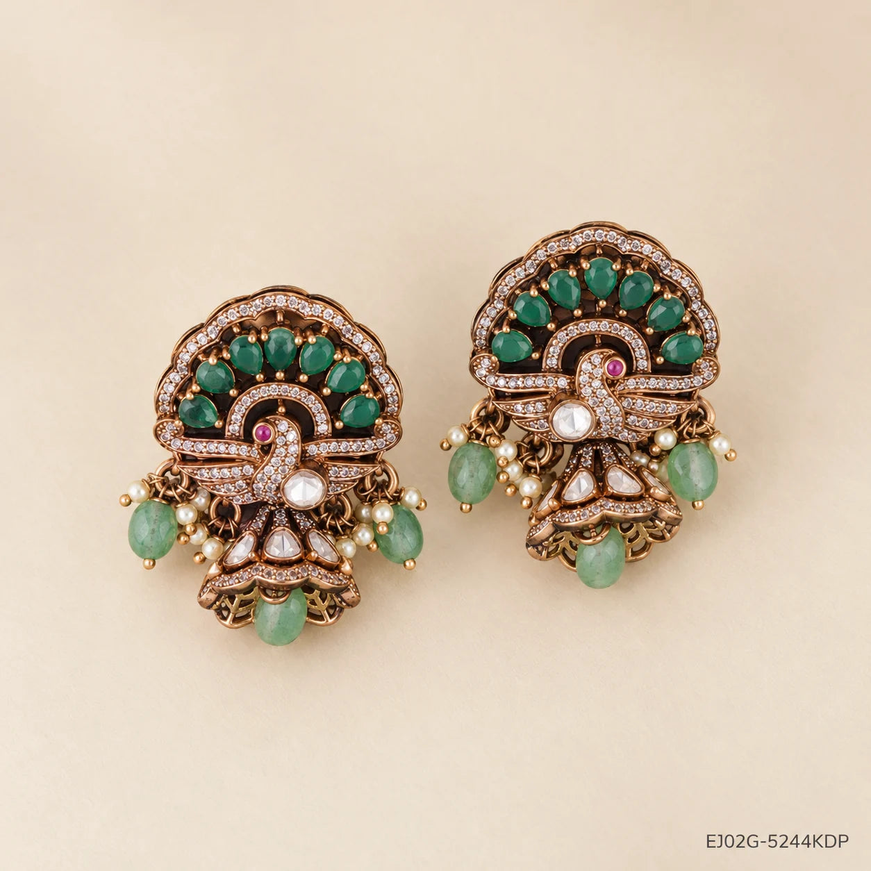 Victorian buttalu earrings with antique finish and green stone drops, placed on beige background
