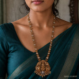 Close-up of a woman's neckline showing the pearl-beaded chain and ornate deity pendant