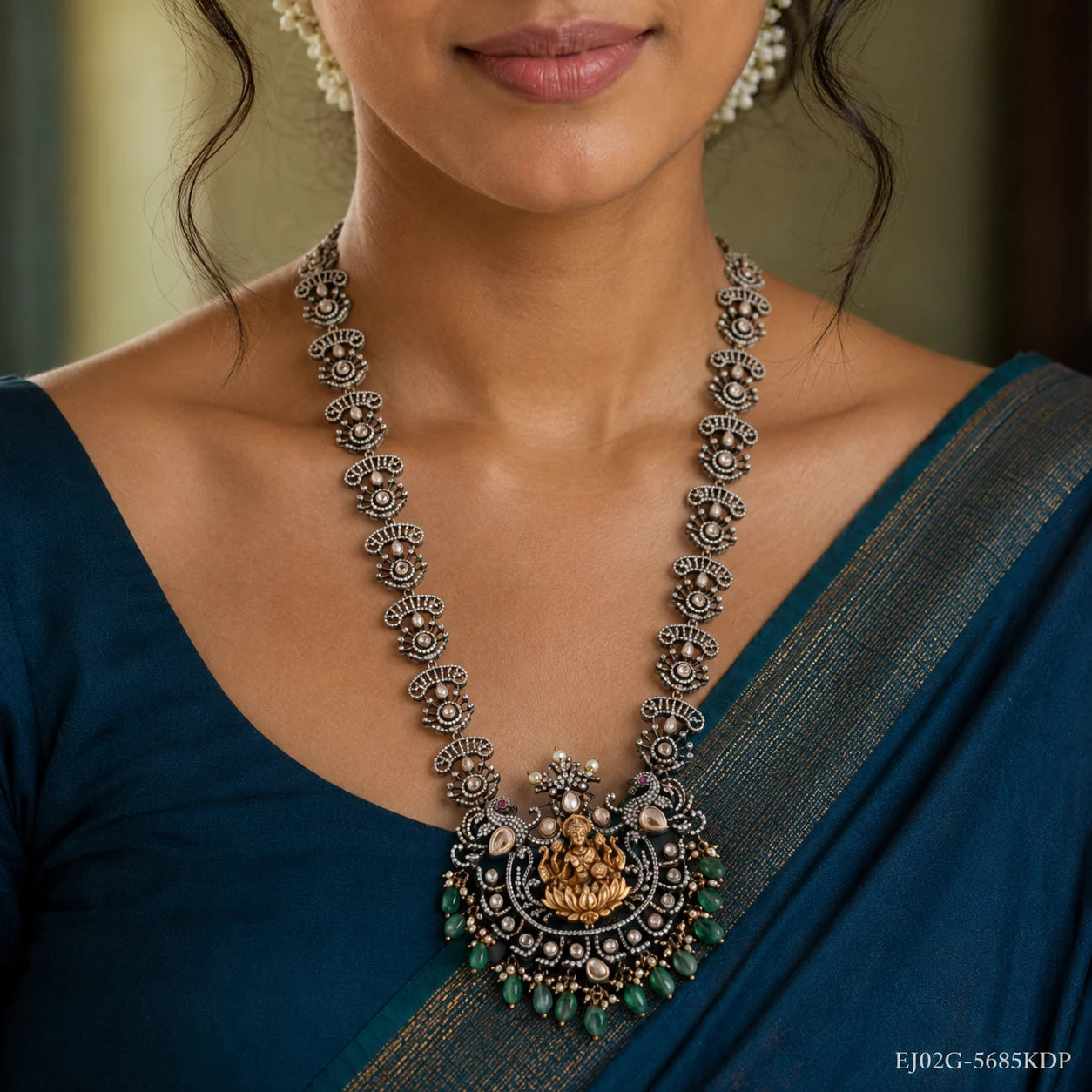 Close up of neckline showing the long necklace chain and detailed pendant with green drops