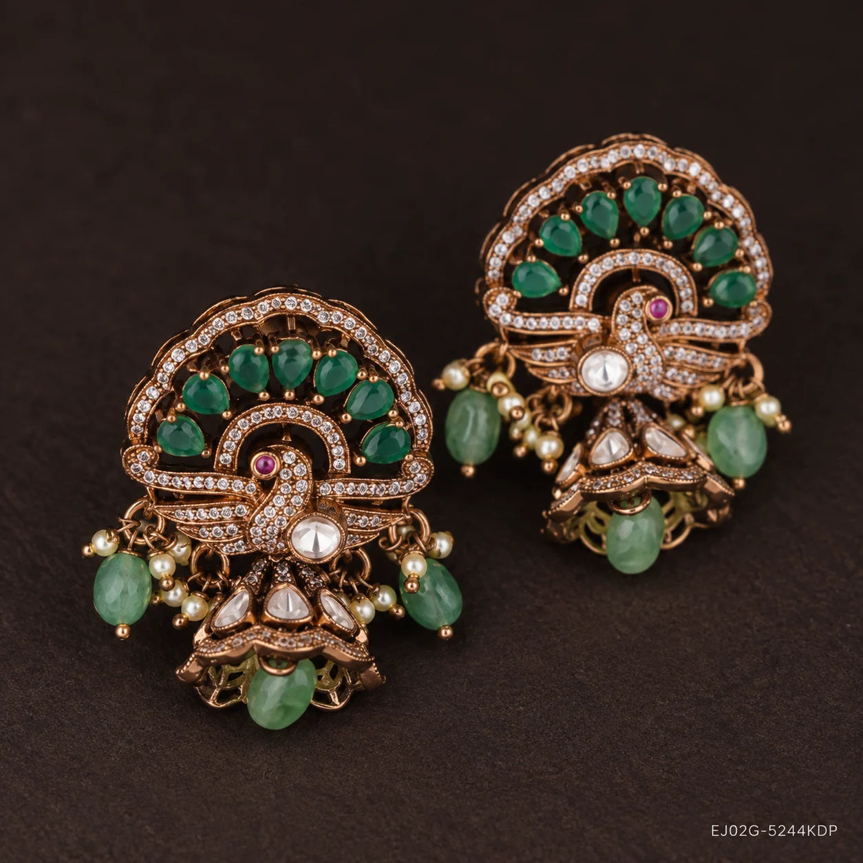 Close-up angled view of peacock design buttalu earrings with green stones and pearl accents on dark background
