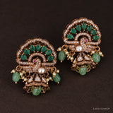 Close-up angled view of peacock design buttalu earrings with green stones and pearl accents on dark background