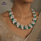 Close up of the necklace on a woman's neckline showing floral white stone clusters alternating with oval green stones