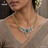 Close-up of neckline showing a gold-tone necklace with CZ floral and leaf motifs and three green stones