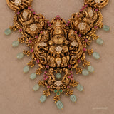 Close-up of the necklace centrepiece showing the carved deity figure, peacock details and pink and green stones