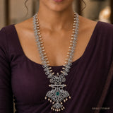 Long necklace displayed on beige fabric beside dried flowers, showing the complete design