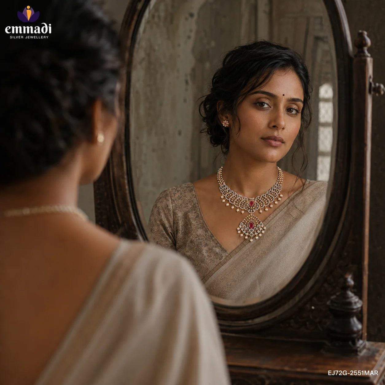 Woman in cream saree looking into an antique mirror wearing a silver paisley necklace with pink stone and pearl drops