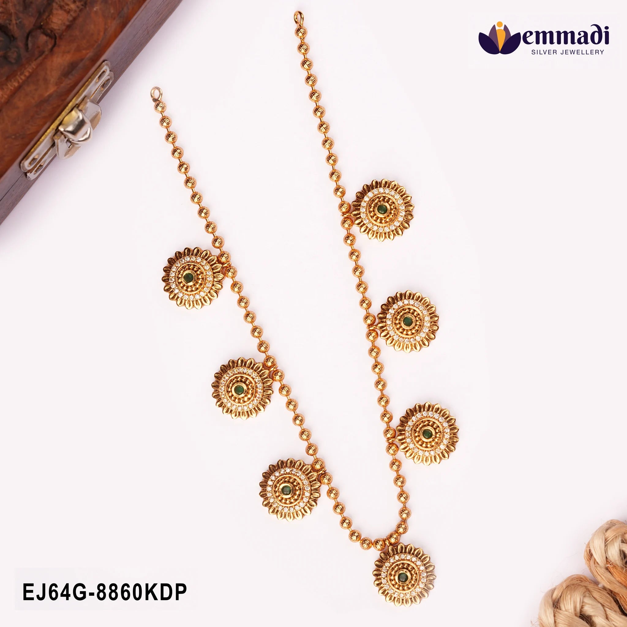 Flatlay of gold-tone beaded necklace with green stone floral medallions beside a wooden box