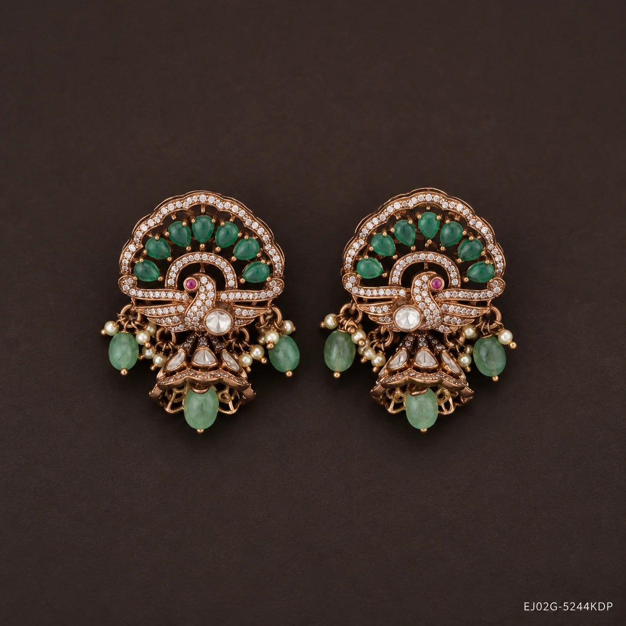 Pair of victorian buttalu earrings with peacock motif, green stone clusters and pearl drops, on dark brown background