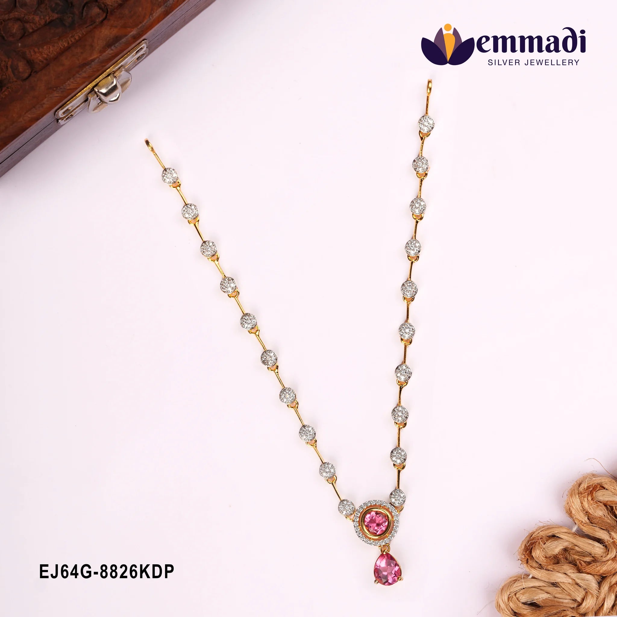 Pink CZ necklace with gold-tone chain laid flat beside a carved wooden box corner