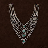 Four-layer silver necklace with green stone pendants laid flat on dark brown fabric