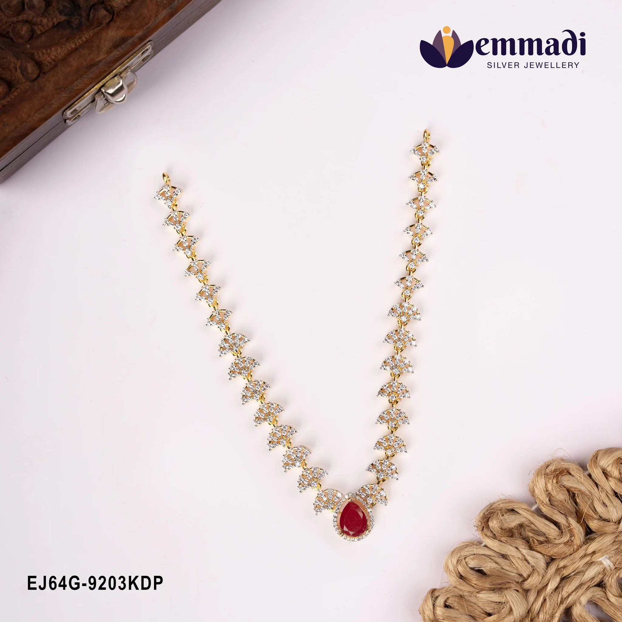 Red and white stone necklace laid on cream fabric beside a carved wooden box