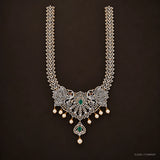 Long necklace with pave cz chain, peacock motifs and green stone pendant on dark brown background