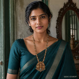 Woman in a teal saree wearing a long antique gold-tone necklace with a carved deity pendant