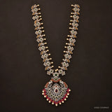 Full view of green long necklace with floral cz links and peacock pendant on dark brown background