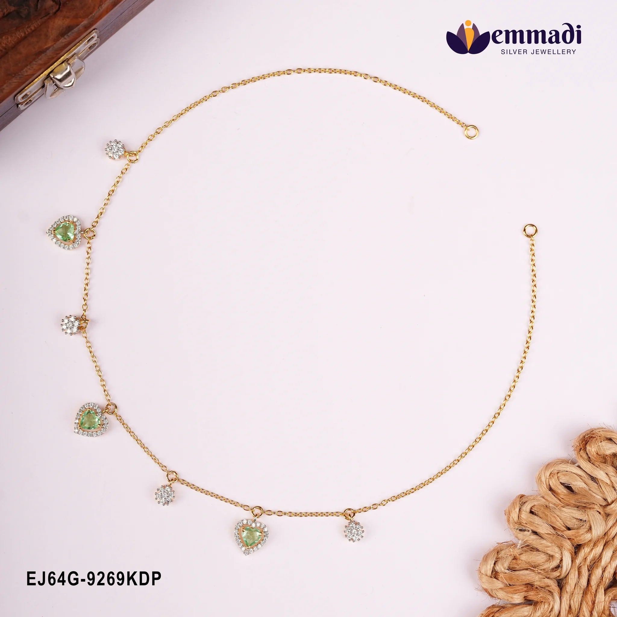 Gold-toned necklace with green heart stone drops and CZ pave charms laid in a circle beside a wooden box