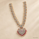 Green long necklace with pearl drops and pink stone pendant laid flat on beige background