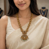 Close-up of the antique necklace resting on the chest, showing the floral pendant with pearl and green drops