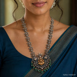 Close up of neckline showing the long necklace chain and detailed pendant with green drops