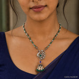 Close-up of peacock pendant necklace with green beads and pearl tassel on navy blue saree
