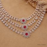 Flat lay of the necklace on beige fabric showing the floral vine strands and red stone centres up close