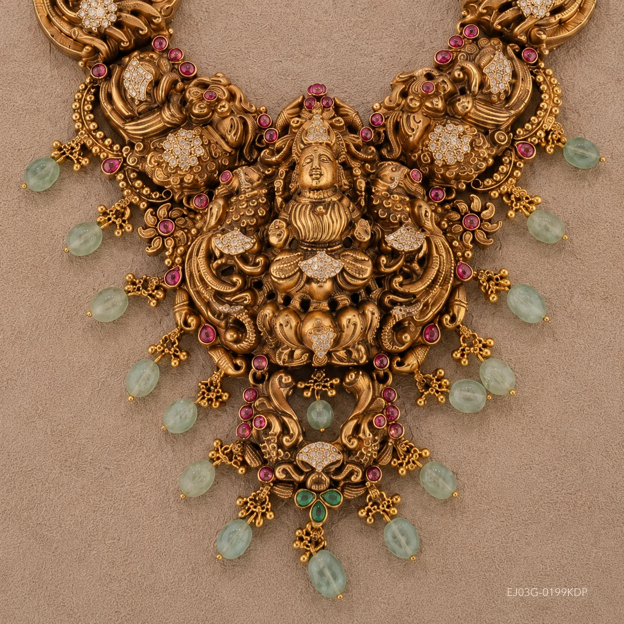 Close-up of the necklace centrepiece showing the carved deity figure, peacock details and pink and green stones