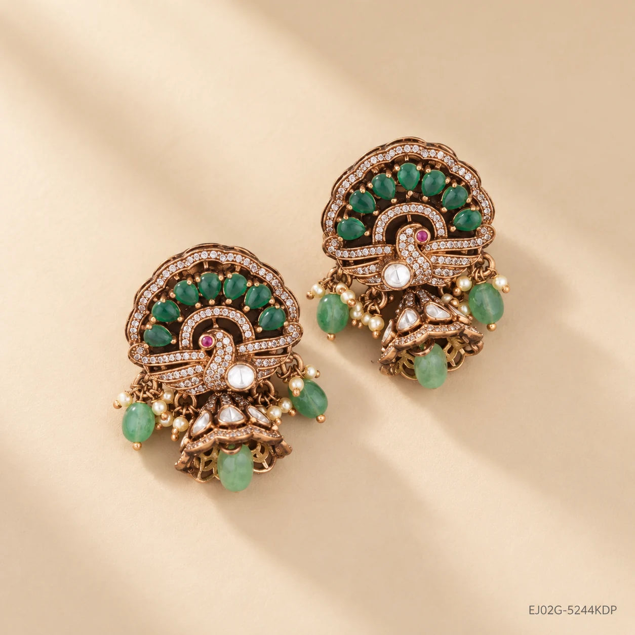 Victorian buttalu earrings with jhumki style base and green stone dangles, on beige background with soft shadow