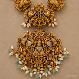 Close-up detail of the pendant showing a carved deity figure, peacock scrollwork and pearl-green bead fringe