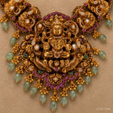 Close-up of the central medallion showing the carved deity figure, pink stones and green bead fringe